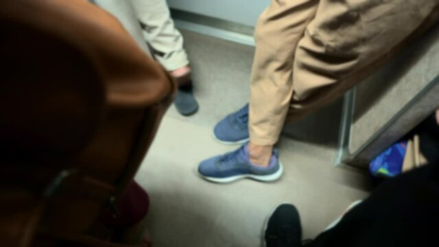 The legs of commuter train passengers crammed together and leaning over at night in Jakarta. Depicts a train full of after-hours workers