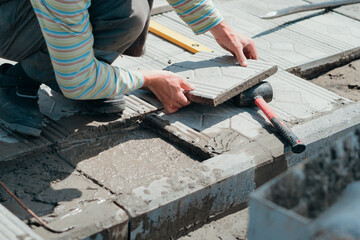 Worker tiler lays tiles with cement outside on summer day. Authentic workflow. Hands with facing tiles.