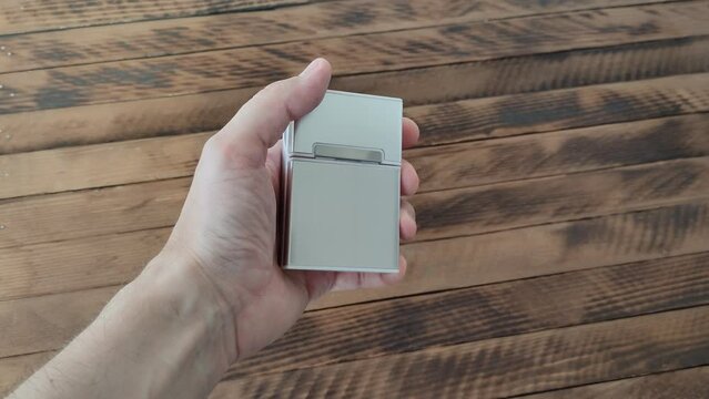 Man holds a metal cigarette case in his hand on a wooden background