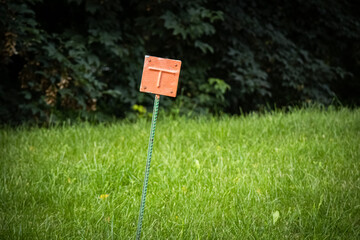 A shifted metal red squared marker indicating the route of a gas pipeline on a street lawn