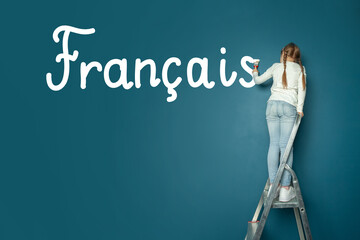 Child student girl standing on ladder and writing French language on blue chalkboard