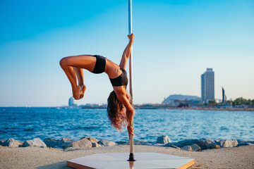 Young beautiful woman pole dancing on sea background