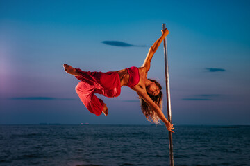 Young woman pole dancing on sea and sky background at twilight