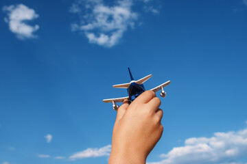 Baby's hand holding toy airplane on sky background, air travel concept