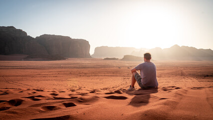 Tourist sitting in red sand watching the romantic and beautiful sunset at Wadi Rum desert, Jordan