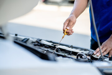 Auto mechanic repairman using tablet and pulling dipstick to checking engine oil level engine in the engine room, check the mileage of the car, oil change, auto maintenance service concept.