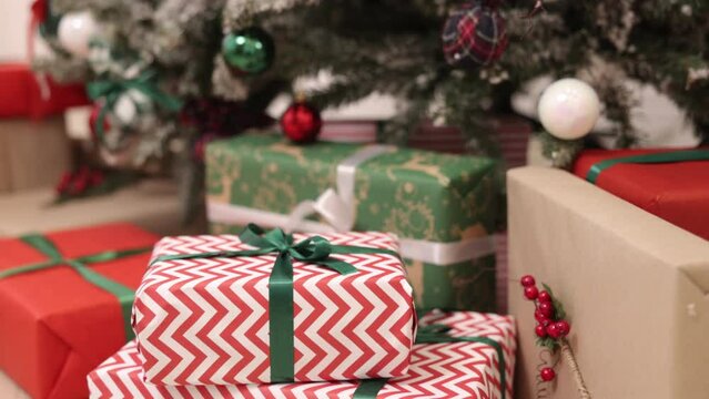 Christmas presents, gift boxes, New Year gift. Gft boxes are tied up with ribbons and decorated with Christmas ornaments. The background is of a fir tree in the room and beautiful Christmas gift boxes