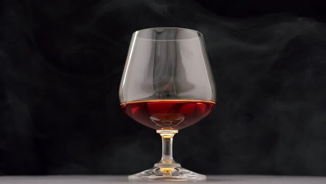 Luxury brandy. Glass with golden cognac on isolated black background with smoke. Brandy, cognac, and whisky. Slow motion. Luxury Drink Whisky with smoke.