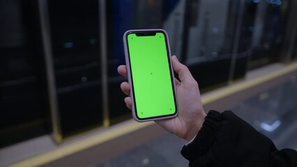 Close-up of a woman's hand with a phone on the background of a passing subway car. Green smartphone screen for your advertising