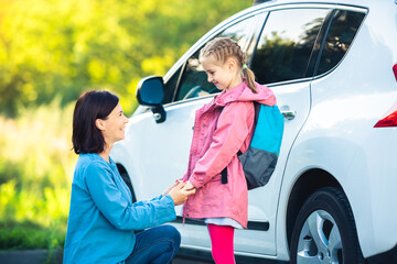 Smiling mother bringing daughter back to school saying goodbye on car parking