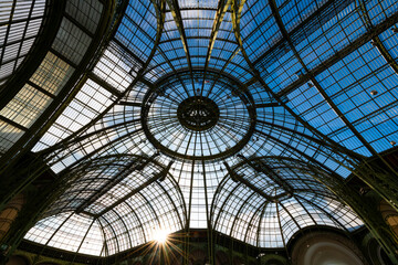 Historic glass roof with steel beam and rivet construction from the 19th century. Blue sky and low sun above the cupola of an old exhibition hall in Paris, France. Architectural masterpiece from below - obrazy, fototapety, plakaty