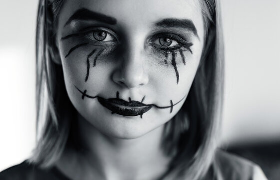 Little girl with spooky Halloween makeup brushed eyes looking at camera. Creepy kid's portrait with crazy joker expression, black and white.
