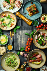 A set of food and dishes in plates. Top view. Food banner. On a dark stone background. - obrazy, fototapety, plakaty
