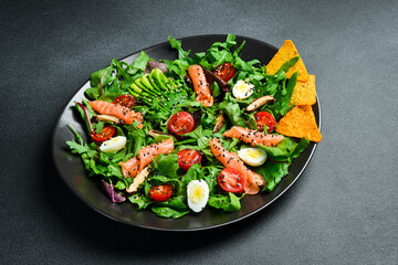 Fresh healthy salad. Salad with arugula, salted salmon, avocado, quail eggs and mushrooms. In a black plate. Diet food.