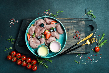 Dumplings with strawberries and sour cream. On a black stone background. In a plate, close-up.