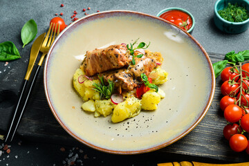 Stewed pork ribs in a cream sauce, with boiled potatoes. On a plate. Restaurant serving. Close up. On a dark stone background.