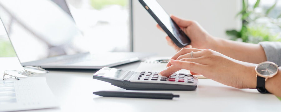 hands of business woman, female entrepreneur using calculator and mobile phone during online working on laptop computer on office table at home, telecommuting, work from home concept