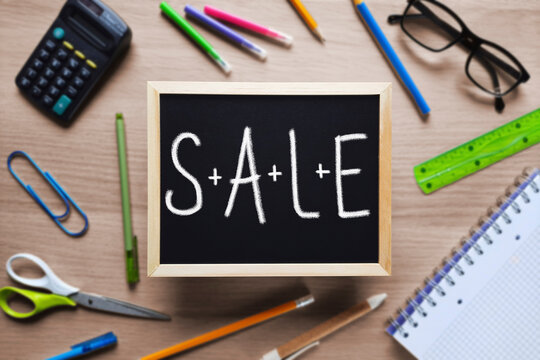 Writing in chalk on board Sale. Message in chalk on blackboard on blurred background of table with school supplies. Top view on flat lay. Back to School Sales. Template for advert, Stationery store