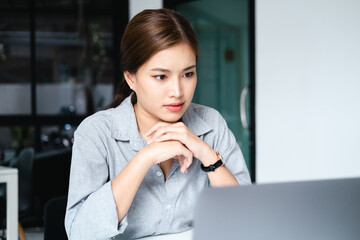 Millennial Asian businesswoman focusing on her project assignment, using laptop computer, working in her office room.