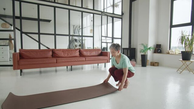 Old woman make yoga exercise at home. Mature woman have meditation. she prepare to exercise sits down on the mat, and is glad that she has time to rest
