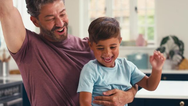 Mature father in kitchen at home with son sitting at counter celebrating after finishing  jigsaw puzzle together - shot in slow motion