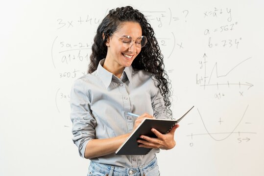 Portrait of young thoughtful Oriental girl student employee leader at modern office university campus looking at note book, making note, project strategy. Curly Arab student with glasses