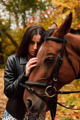 A beautiful young brunette kisses a horse. Autumn forest. Love for animals