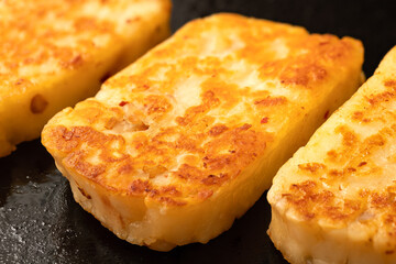 Detail of fried slices of halloumi cheese with red chilli on black frying pan.