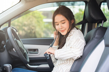 Fototapeta na wymiar Happy smile brunette asian young woman hand fastens a seat belt sitting in front of car before driving, vehicle for travel, trip take a safe journey, attractive driver with safety belt, transportation