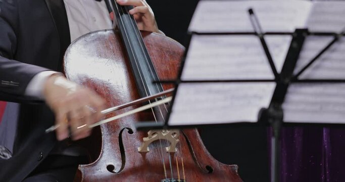 The cellist plays at a concert with excellent stage lighting in close-up. Score with notes in front of the performer.