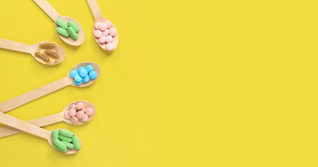 Vitamins on a yellow background, top view. Pills of different colors in wooden spoons, flat lay. Medicines, vitamins and dietary supplements. Banner with place for text