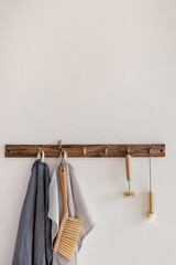 Wood hook rack with tea towels, broom and dish bottle brush hanging on a white wall on the modern style kitchen background. Smart organisation storage ideas. Eco friendly life. Natural materials.