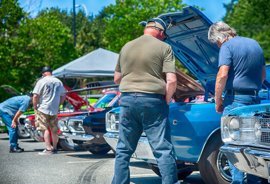 Fototapeta Men view classic muscle cars at outdoor vintage automobile show.
