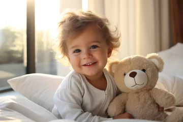 Fotobehang A young child in pristine pajamas enjoying morning play on the bed with a teddy bear. © Usmanify
