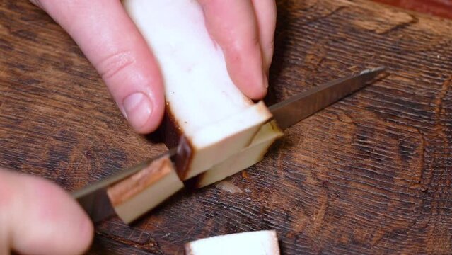 Slicing of salted pork fatback on cutting board, close-up