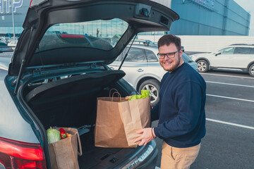 happy man put groceries bag in car trunk