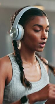 Fitness, headphone and a woman with a watch at gym for running, progress and time. Indian athlete person listening to music, podcast or audio on health app for exercise motivation, focus and wellness