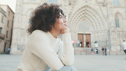 Young smiling woman is sitting on the square of the old city. Tourist rests sitting on the square in Barcelona