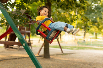 Obraz premium Joyful Japanese Baby Girl Swinging On Swings At Outdoor Playground