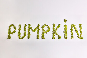 English word PUMPKIN is laid out on a white background of dried green pumpkin seeds. On a gray...