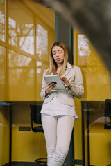 Beautiful blonde girl is checking something on her tablet at the phone booth