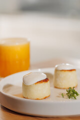 Closeup sweet syrniki, cottage cheese pancakes with white sauce, condensed milk. Healthy nutritious breakfast with orange juice
