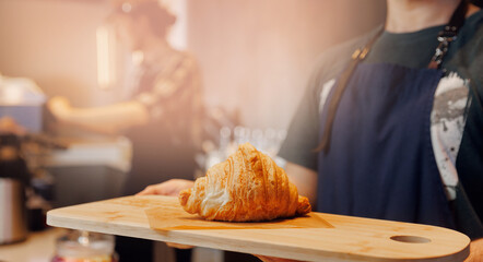 Barista holding fresh croissant on wood table