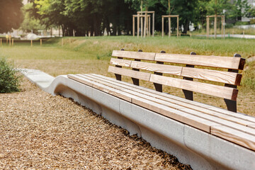 Bench in Green Park with Wood Chips Covering Ground at Children Playground. Modern Wooden Bench in Relax Zone Area on Nature Background.