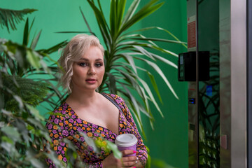 Portrait of beautiful plus size caucasian blonde woman standing with pink paper coffee cup next to...