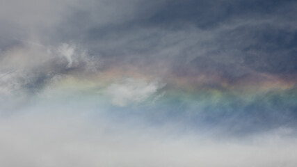 Obraz premium Cirrus clouds catch refracted light creating a short horizontal section of rainbow in the thin wispy clouds.