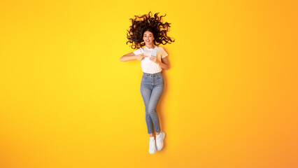 Fototapeta na wymiar Cheerful Woman Pointing At Cellphone Over Yellow Studio Background, Panorama