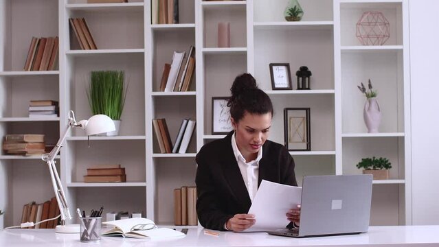 African American girl reads documents and rejoices, happiness, she won. Throws papers. Her company receives new funding. Hispanic latin business lady in black jacket works freelance on a laptop comput