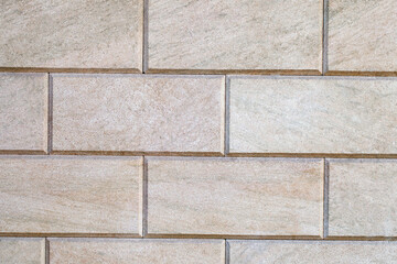 Wall is linked with decorative rectangular beige tiles, close-up, uniform texture background