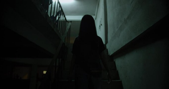 Horror scene of a mysterious Scary Asian ghost woman creepy have hair covering the face walking down on staircase at abandoned house with dark scene movie at night, festival Halloween concept